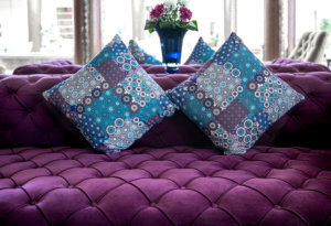 Purple velvet fabric modern sofa with sunken buttons and colorful decorative pillows.